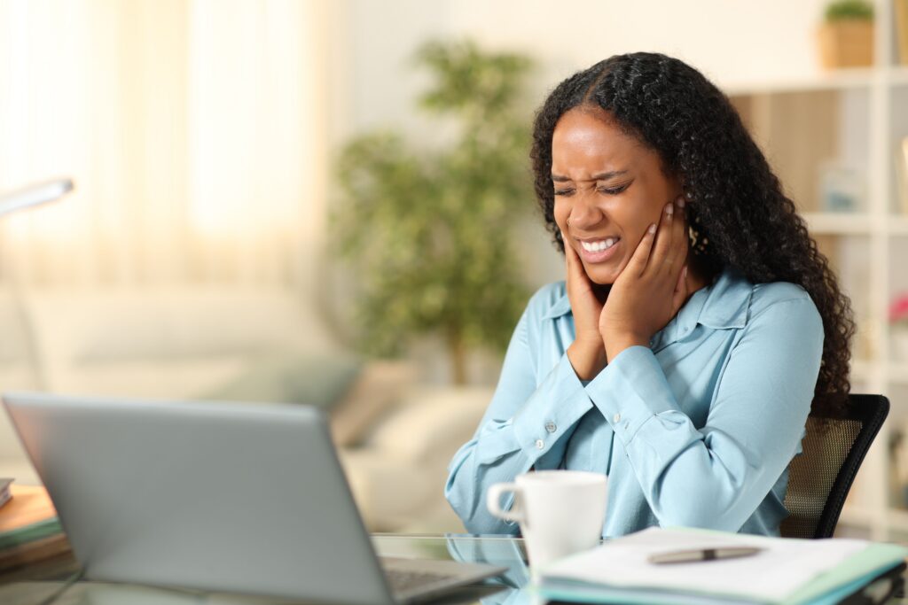 Woman experiencing dental pain while working at a laptop